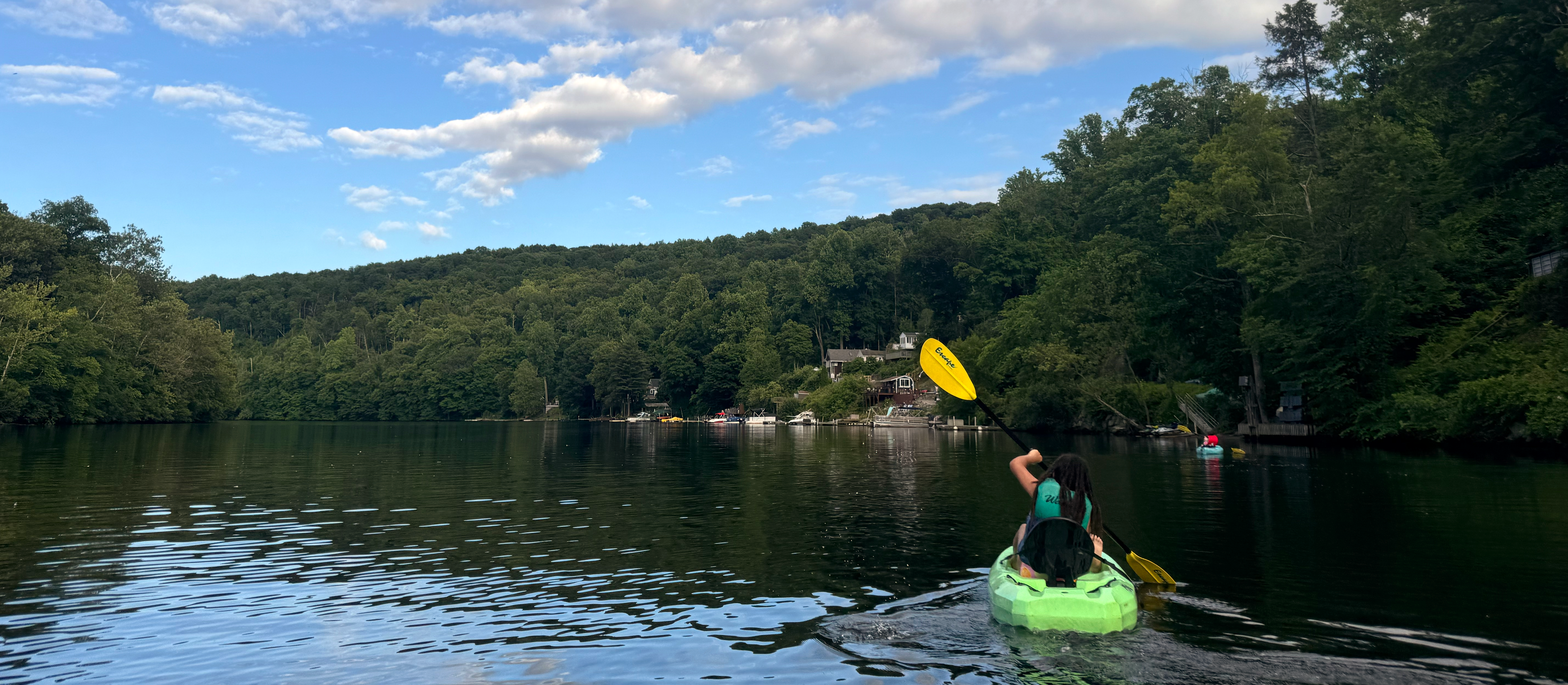Young girl kayaking on Lake Zoar surrounded by trees under a blue sky